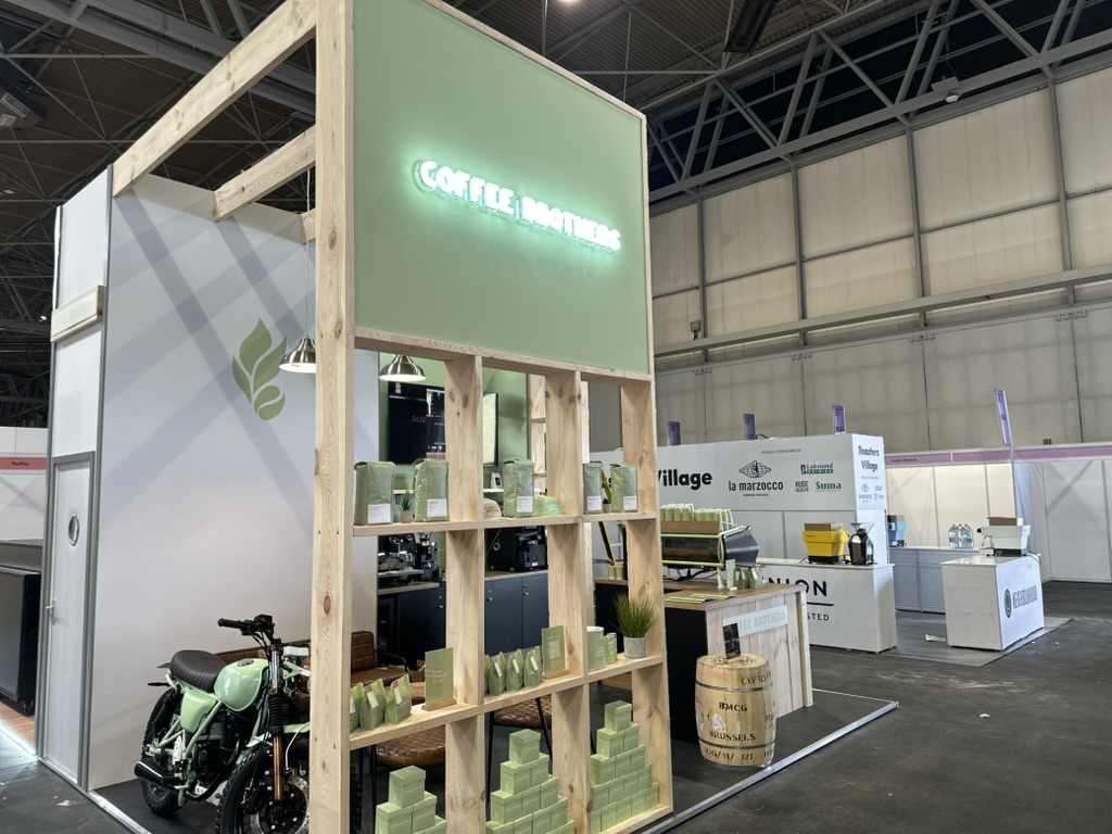 Coffee Brothers exhibition stand with sage green branding, neon signage, wooden shelving and vintage motorcycle